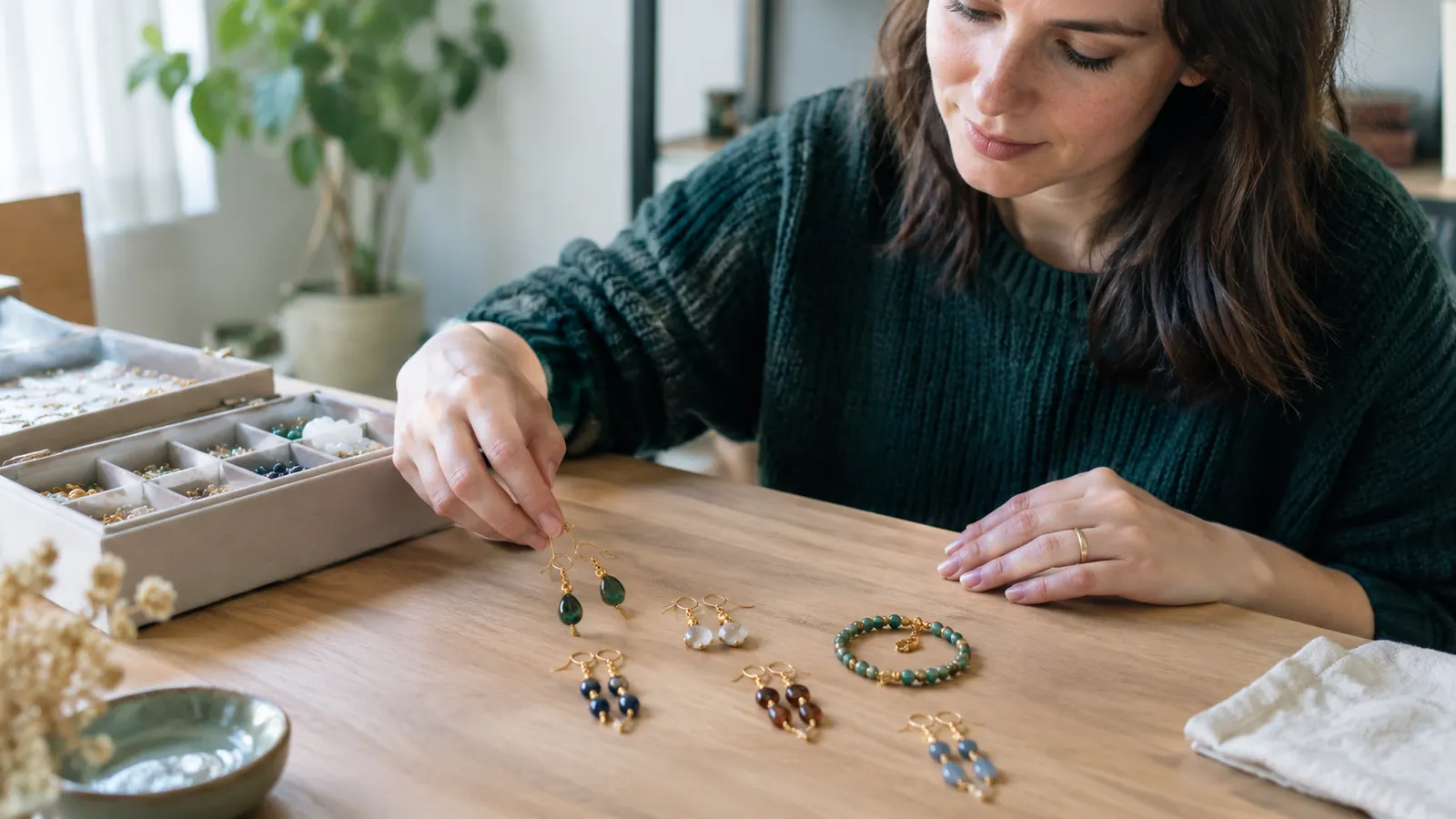 A woman at a craft table laying out finished earrings and a bracelet beside the open kit box